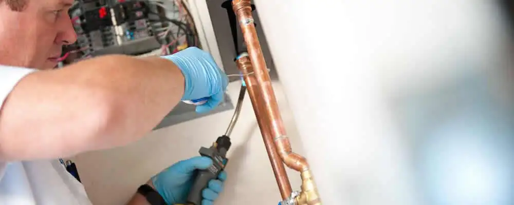 Water heater repair technician testing copper pipe connections and controls in Allentown, PA